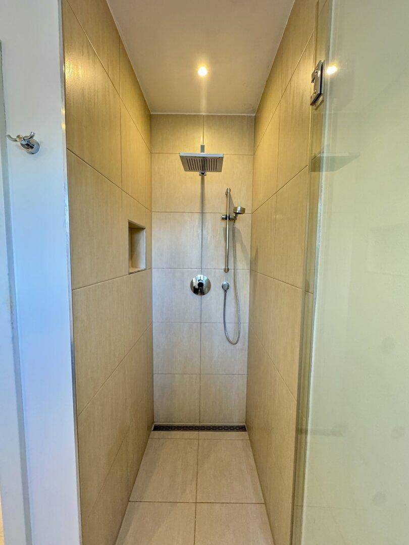 Moderne begehbare Dusche mit beigen Fliesen und Regenduschkopf.