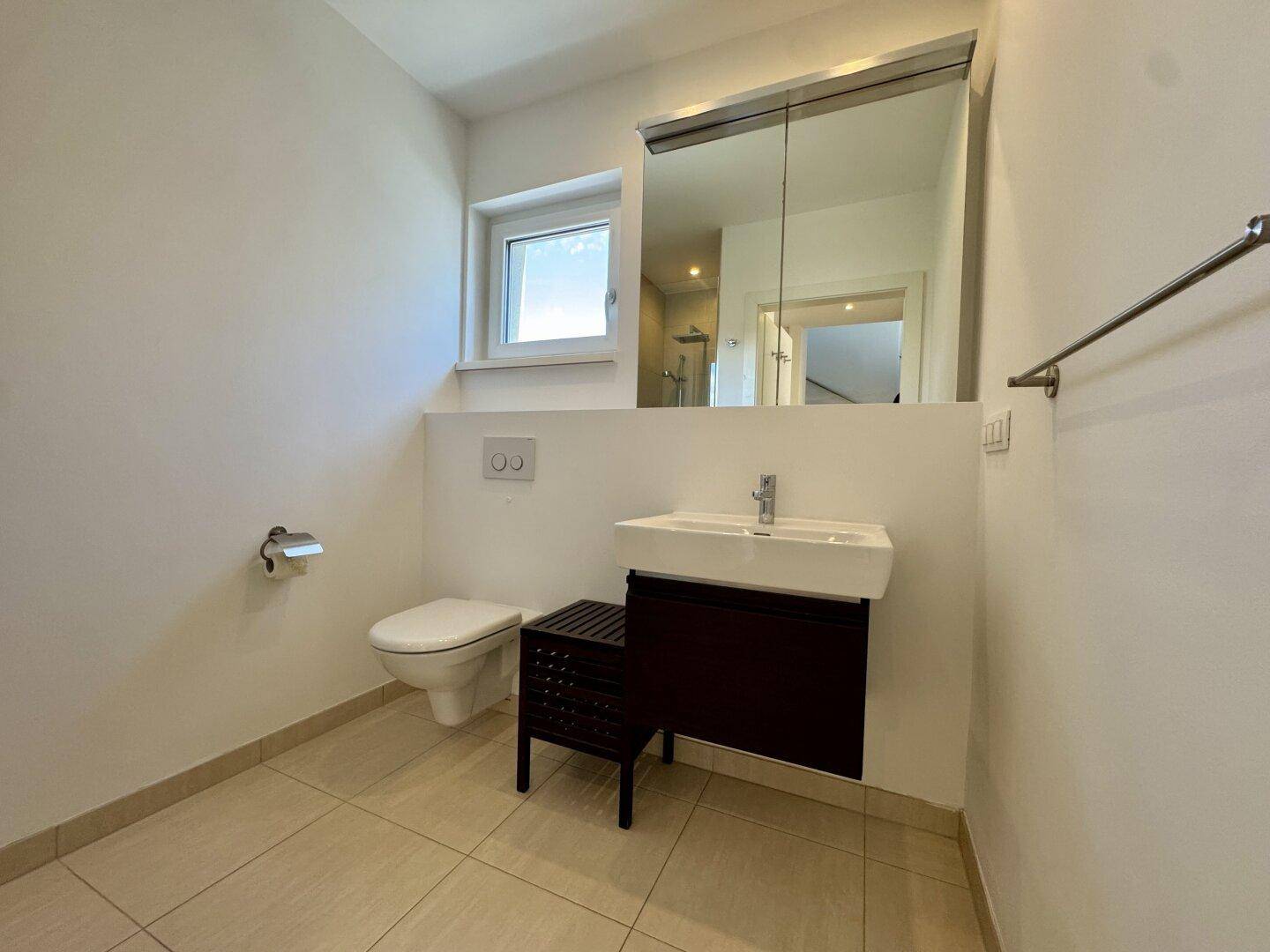 Modernes Badezimmer mit Fliesenboden, Waschbecken, Toilette und Spiegelschrank.