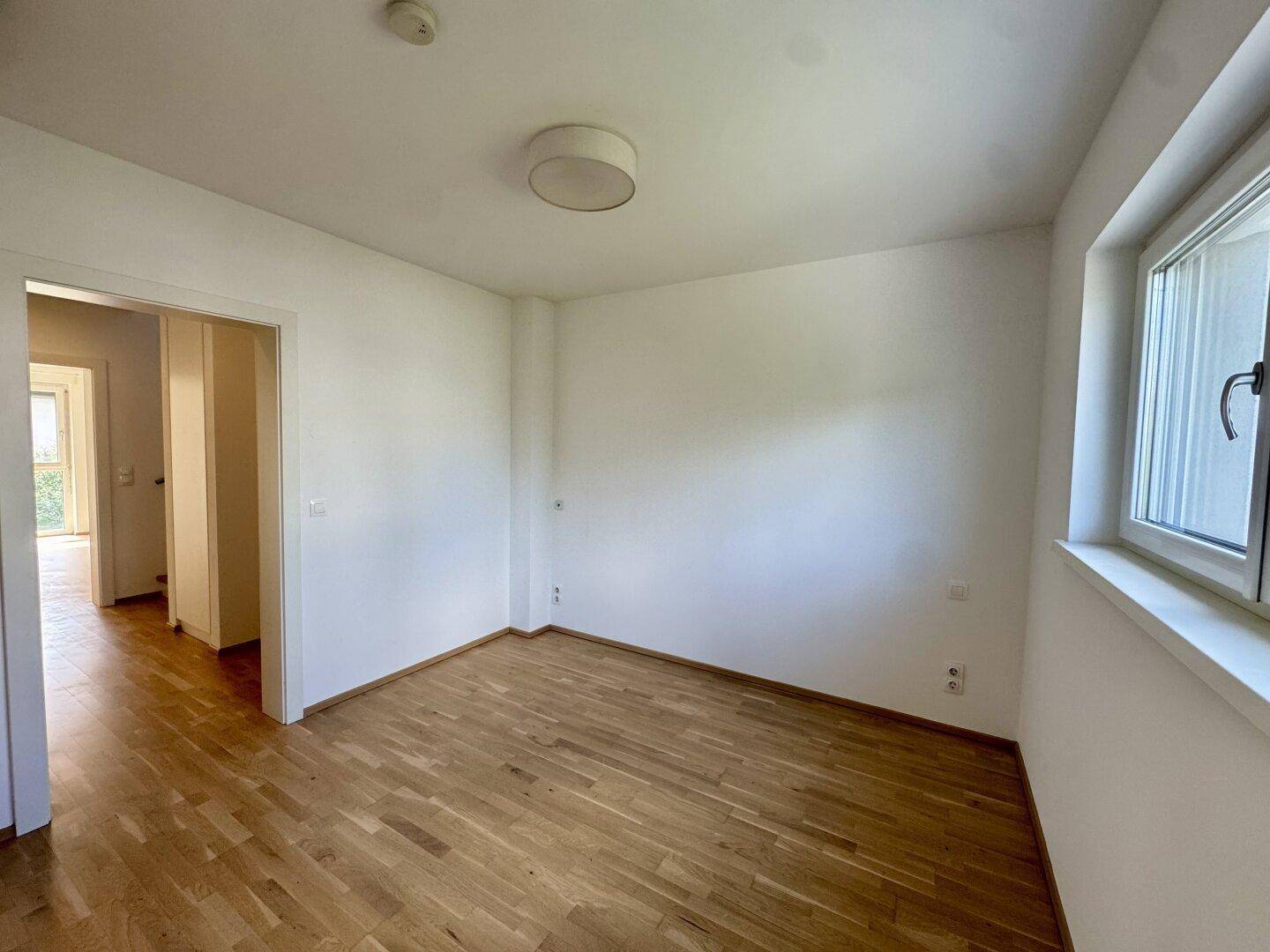Helles Zimmer mit Parkettboden und Zugang zu einem weiteren Raum.