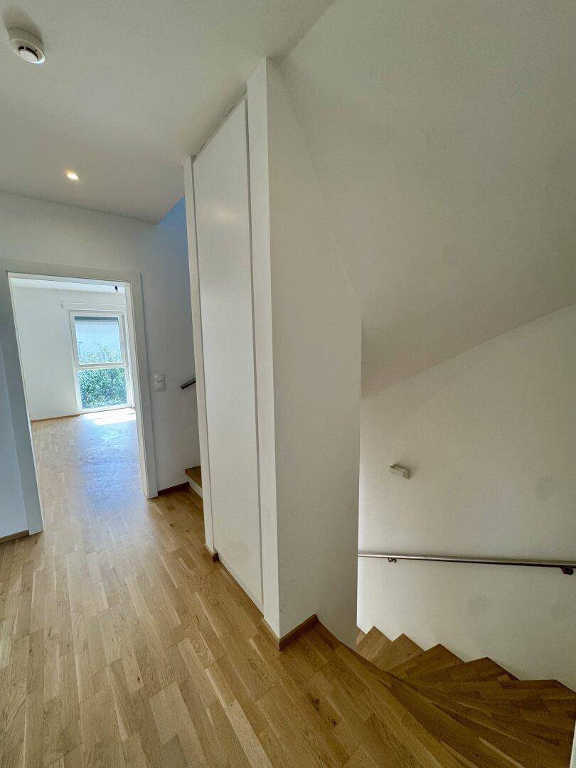 Heller Flur mit Holztreppe und Parkettboden, der zu weiteren Räumen führt.