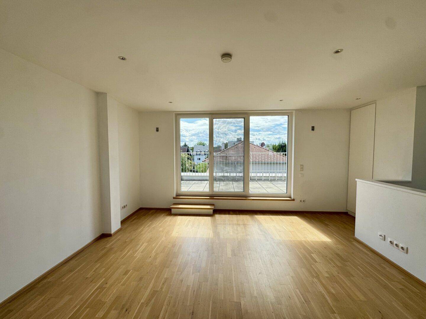 Geräumiges Wohnzimmer mit Parkettboden und großem Fenster mit Zugang zur Terrasse.