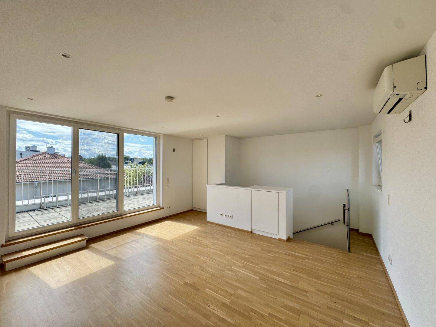 Helles Wohnzimmer mit Parkettboden, Klimaanlage und Zugang zu einer Dachterrasse.