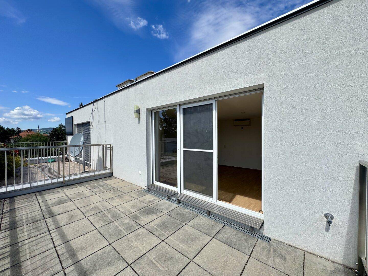 Große Dachterrasse mit Fliesenboden und Metallgeländer, bietet Zugang zu einem Innenraum.