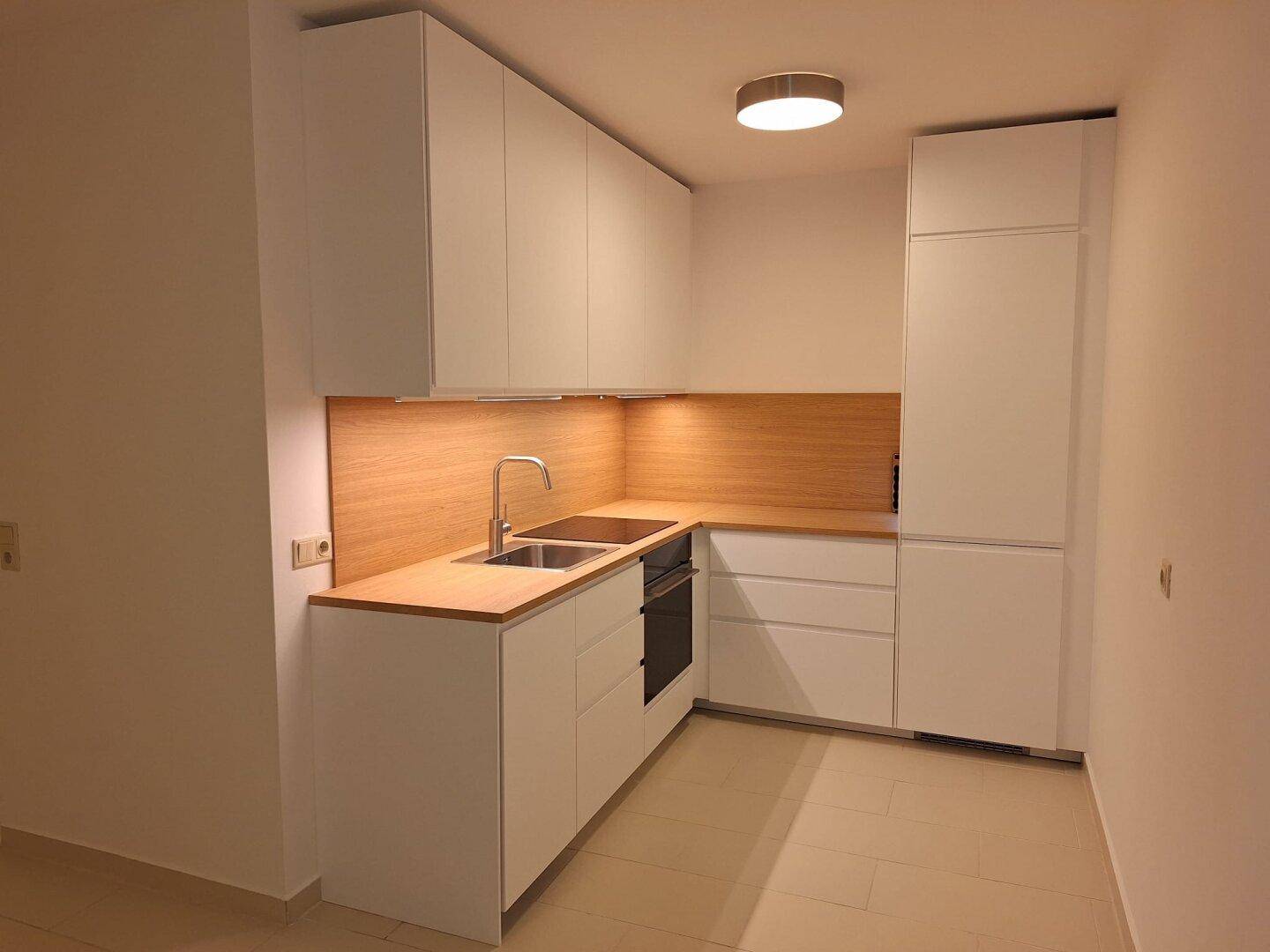 Moderne Einbauküche mit weißen Schränken, Holzdetails und integrierten Geräten.