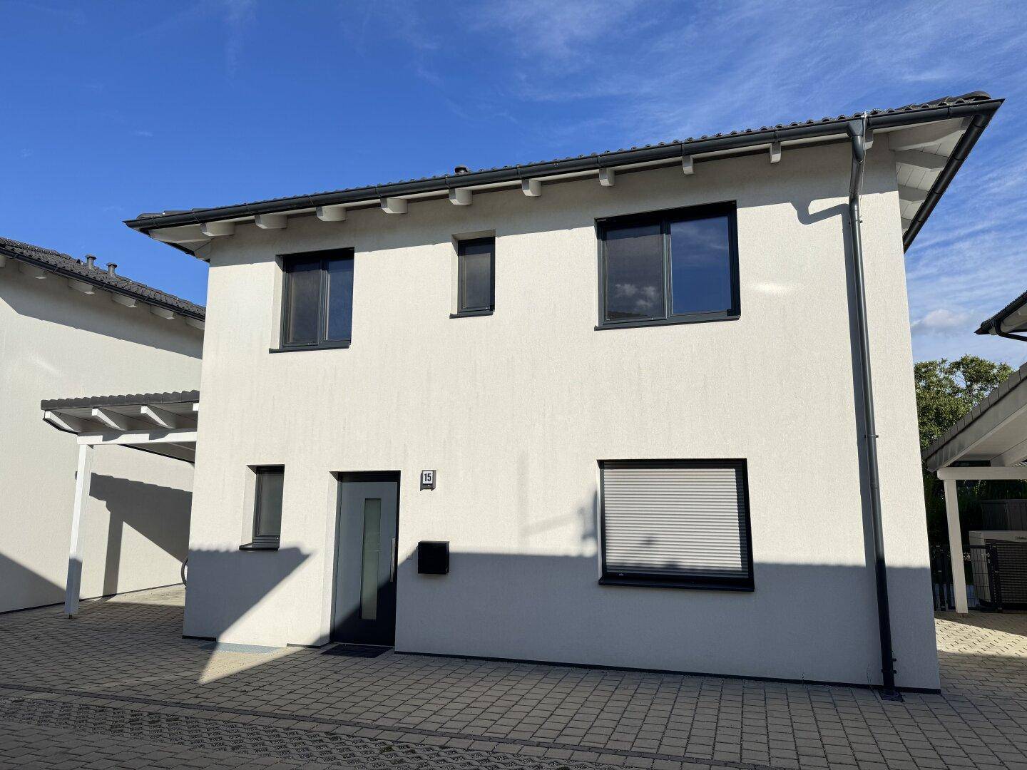 Moderne Hausfassade mit weißen Wänden, dunklen Fenstern und einem Carport auf der rechten Seite.