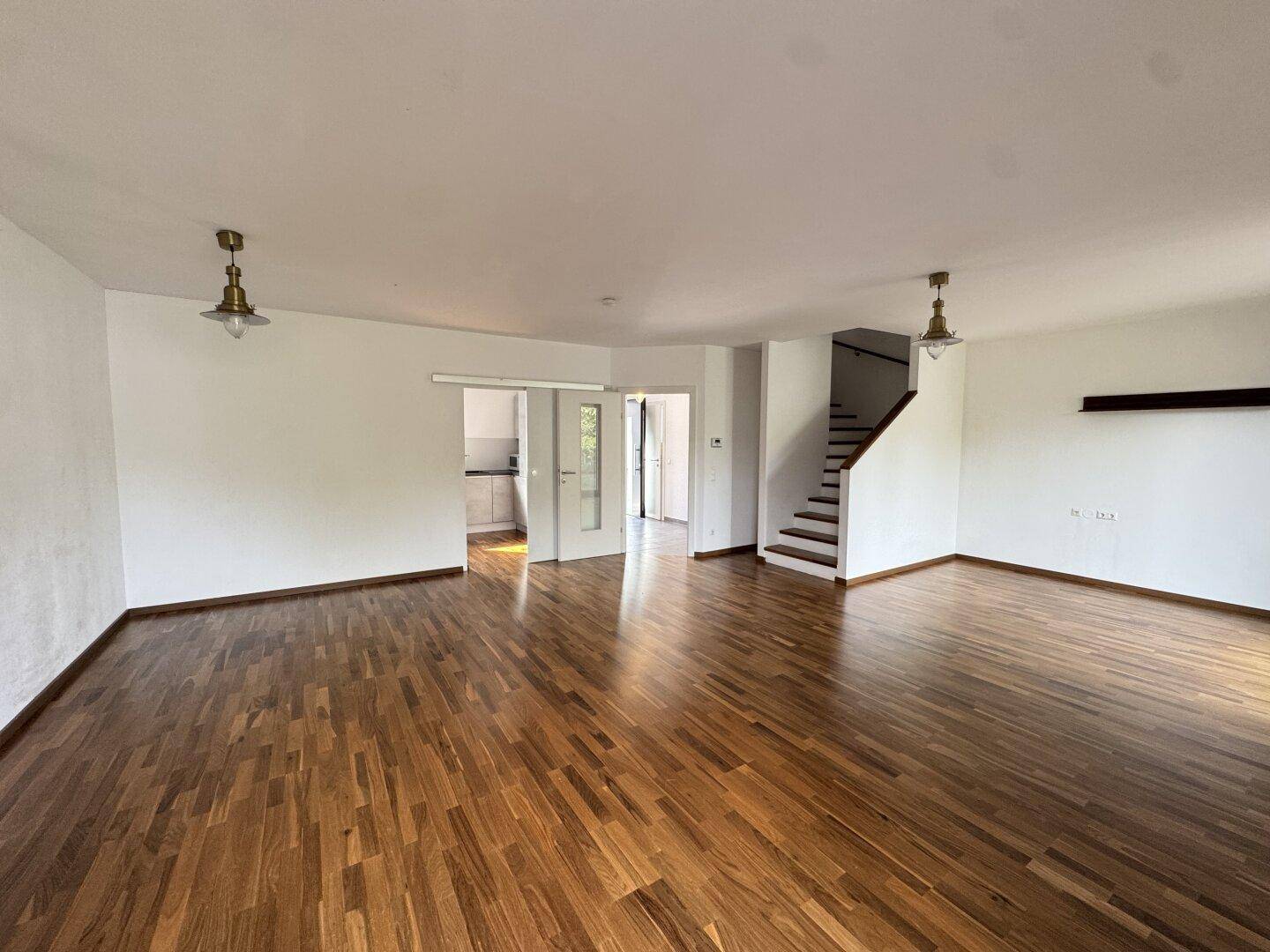 Großes Wohnzimmer mit Parkettboden, Treppe und Blick zum Eingangsbereich.