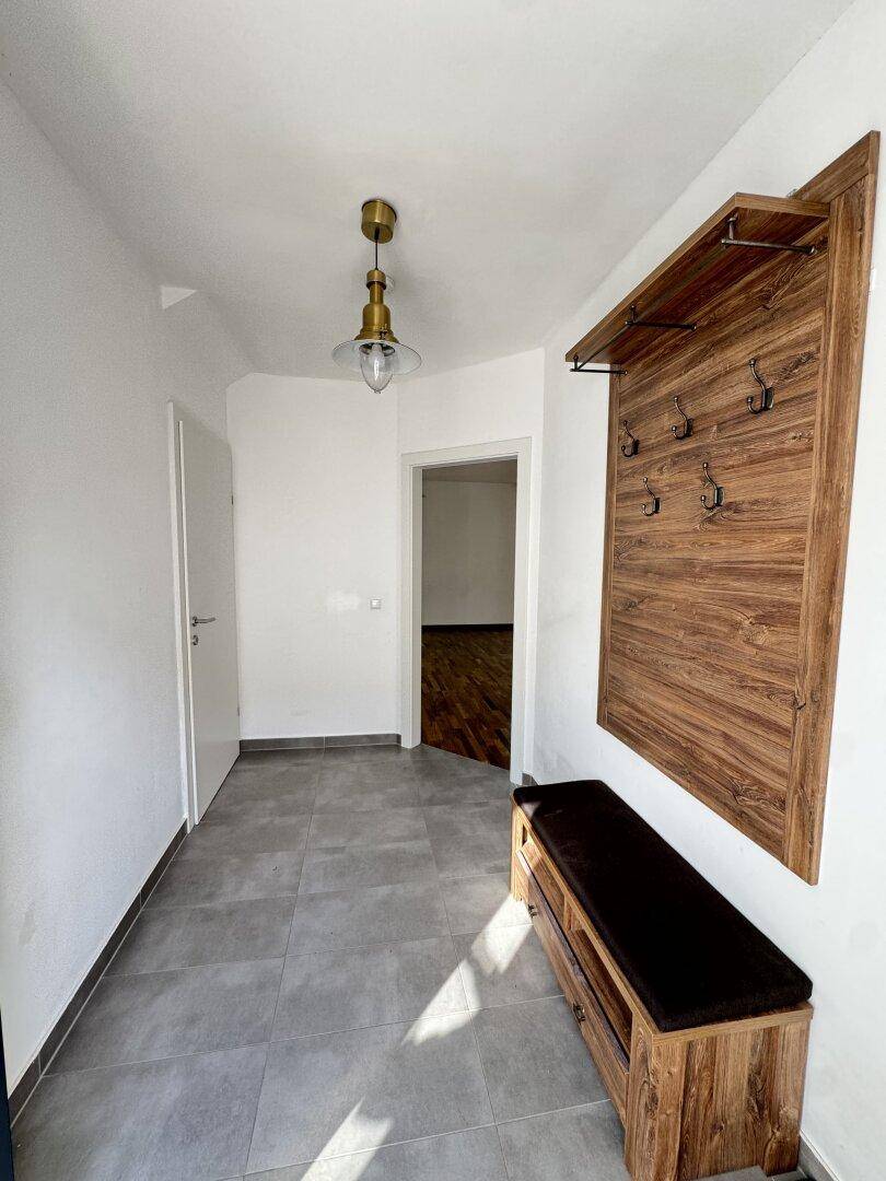Heller Eingangsbereich mit Fliesenboden und Garderobe aus Holz.