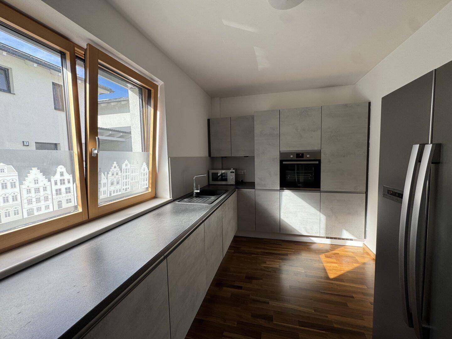 Moderne Küche mit grauen Fronten, Holzboden und großem Fenster.