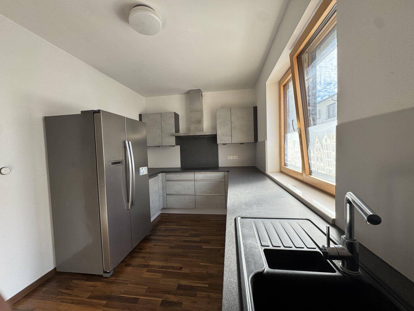 Funktionale Küche mit Edelstahlkühlschrank, Dunstabzugshaube und viel Arbeitsfläche.