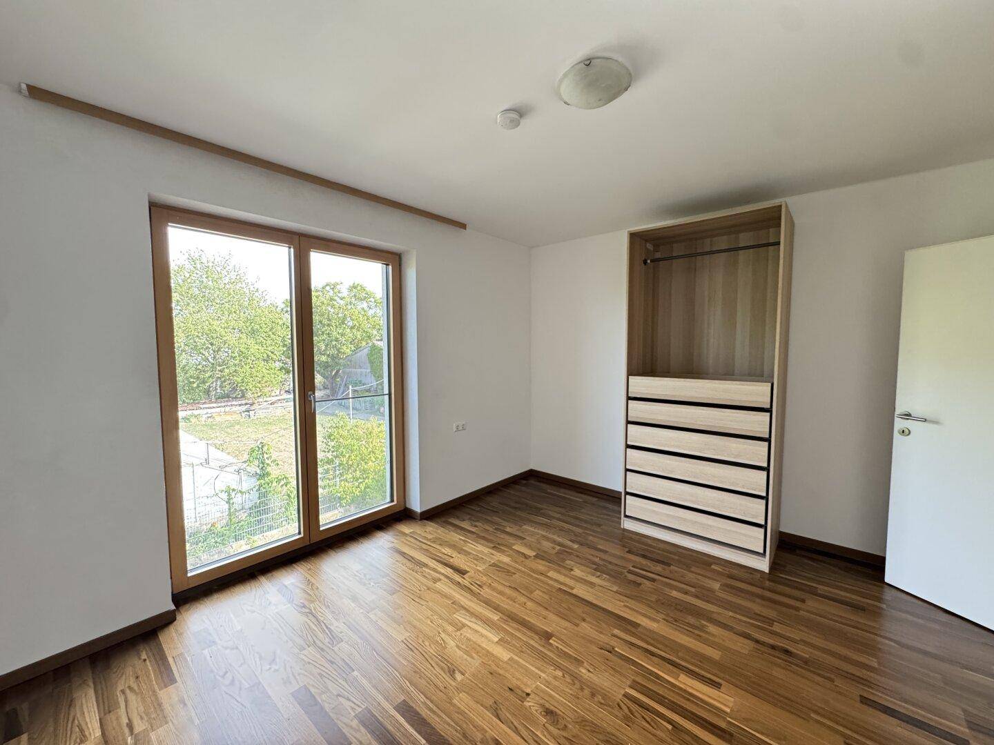 Helles Schlafzimmer mit Parkettboden und offenem Kleiderschrank.