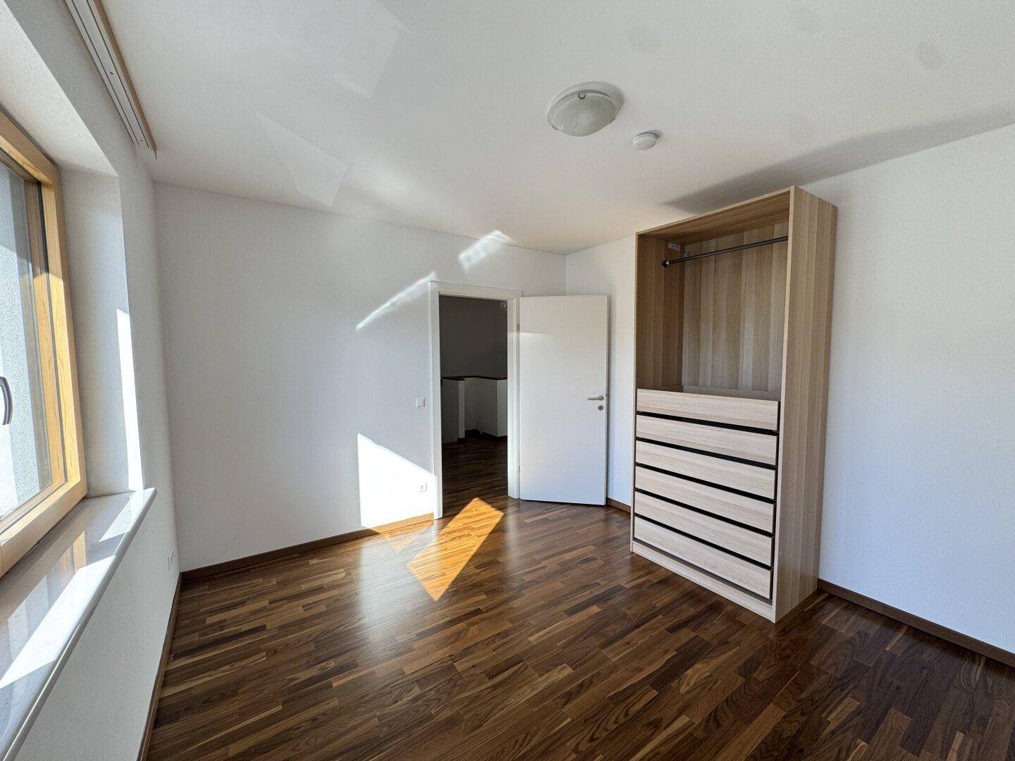 Helles Schlafzimmer mit Parkettboden und offenem Kleiderschrank, sonnendurchflutet.