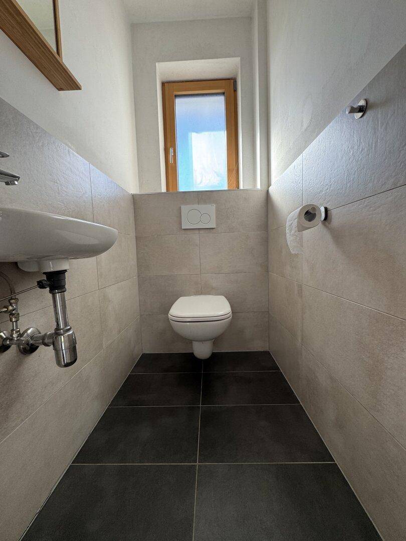 Schlichtes Gäste-WC mit Wand-WC, kleinem Waschbecken und Fenster.