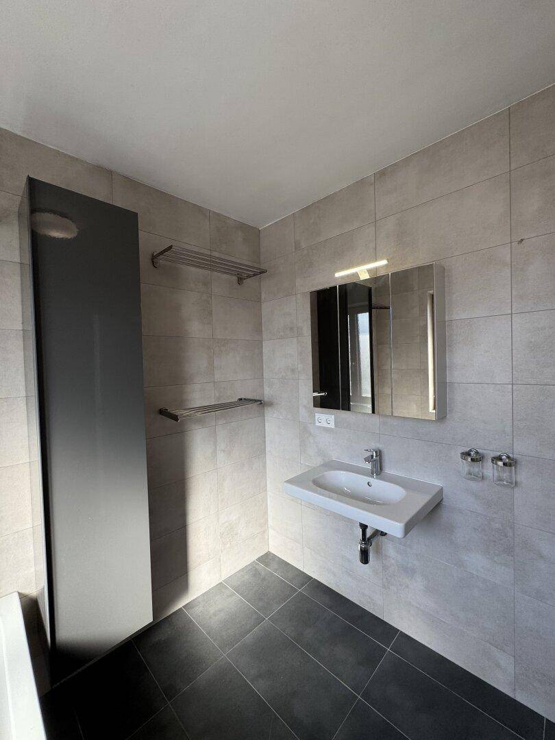Helles Badezimmer mit Waschbecken, Spiegelschrank und Handtuchhaltern.