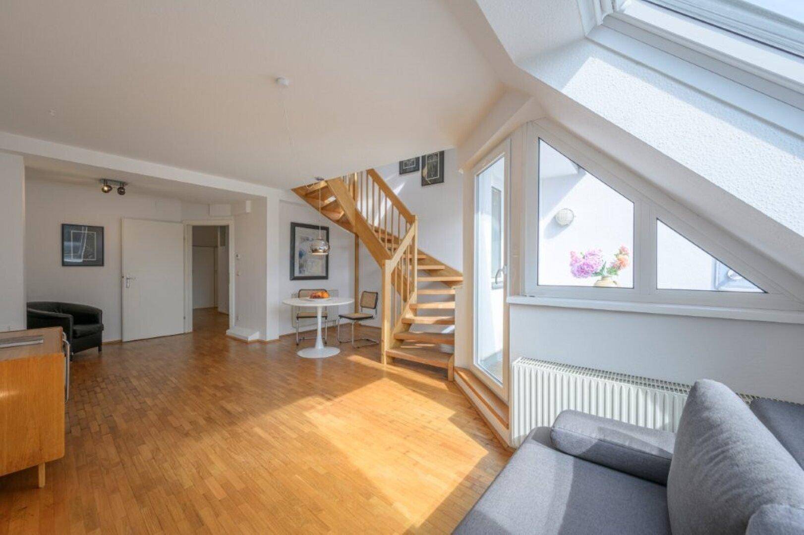 Geräumiges Wohnzimmer mit Parkettboden, Dachfenstern und Zugang zum Balkon.