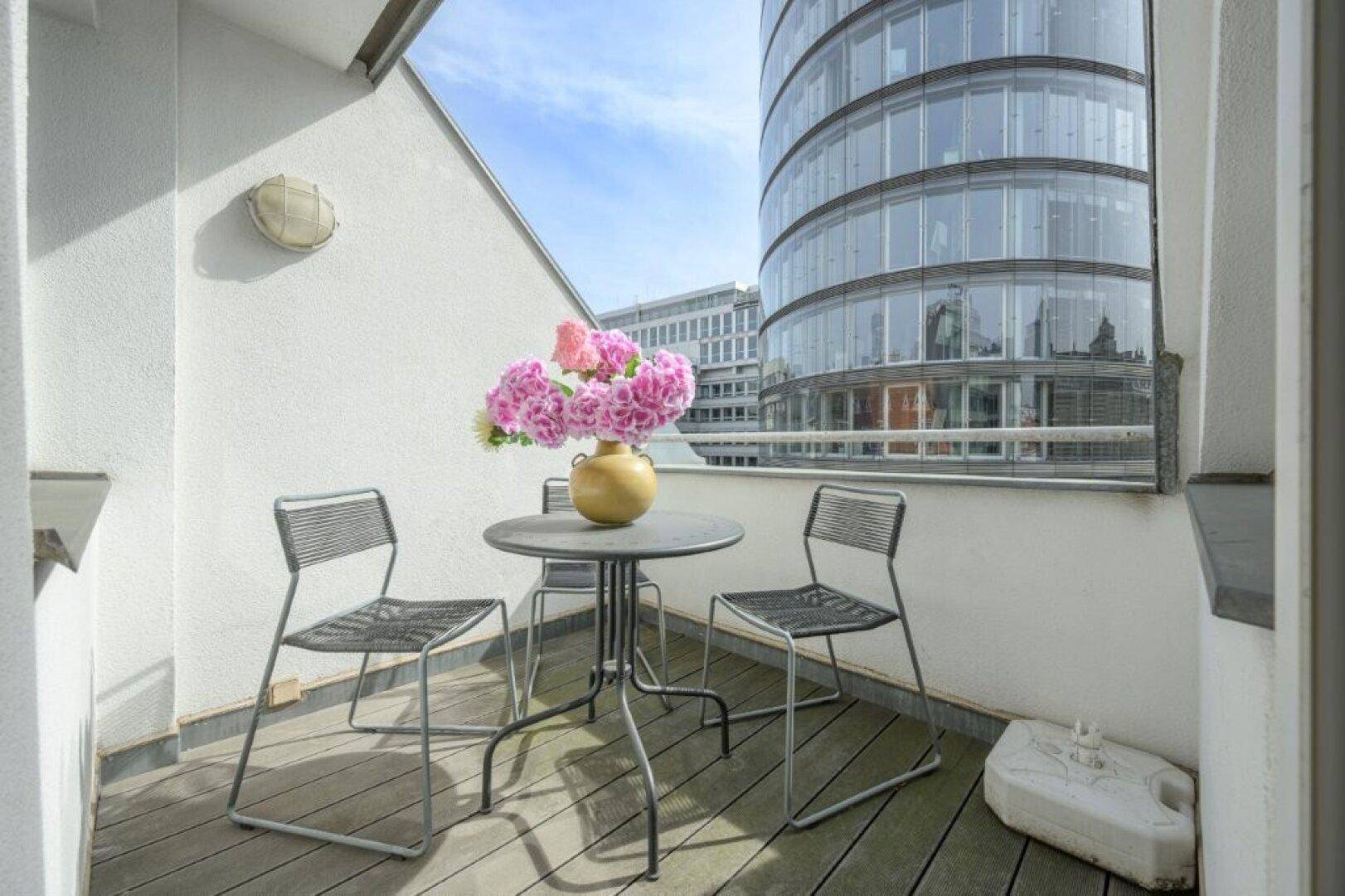 Kleiner Balkon mit Sitzgelegenheiten und Blick auf moderne Stadtarchitektur.