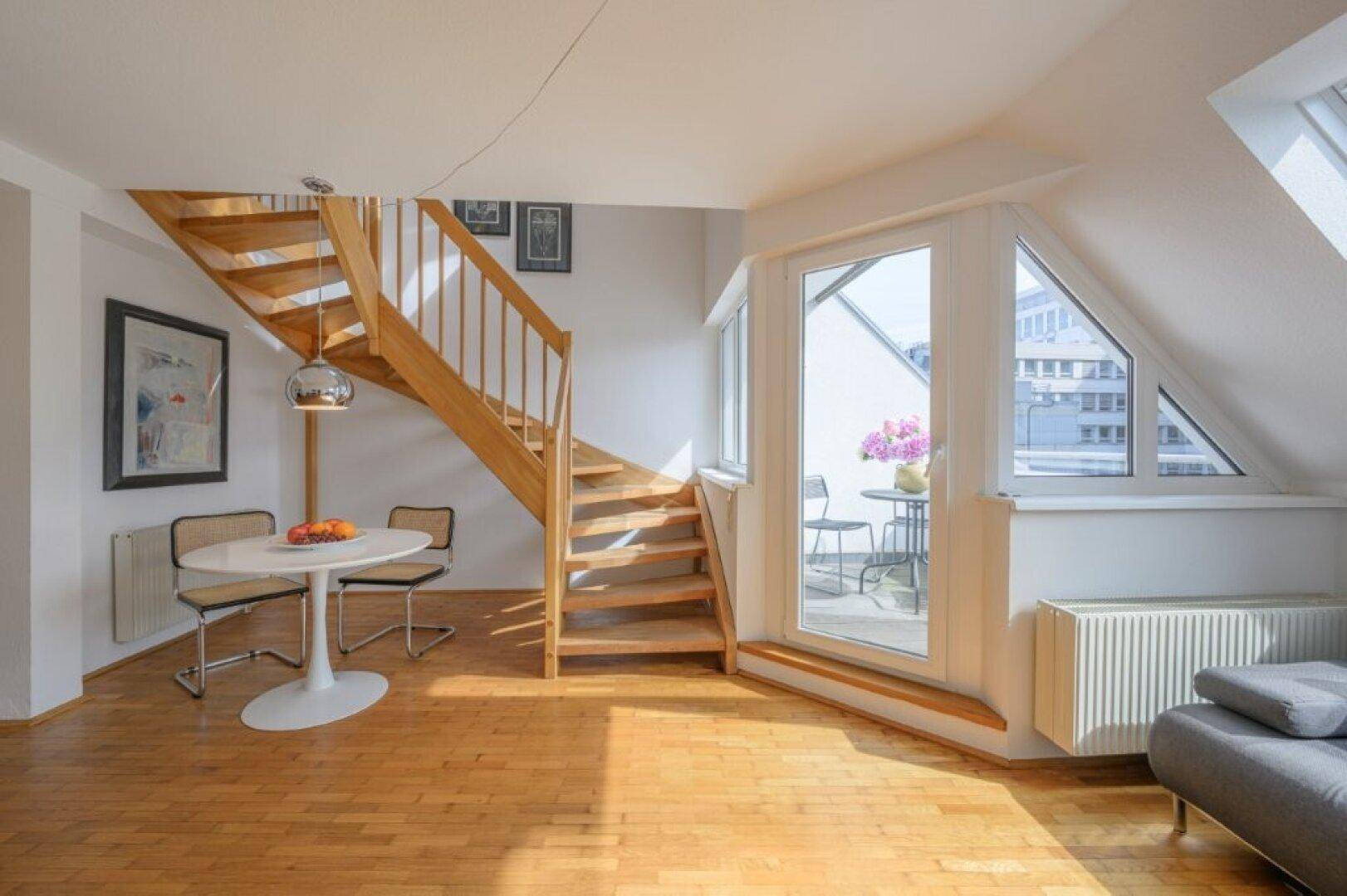 Heller Wohnbereich mit Holztreppe, Esstisch und Balkonzugang.