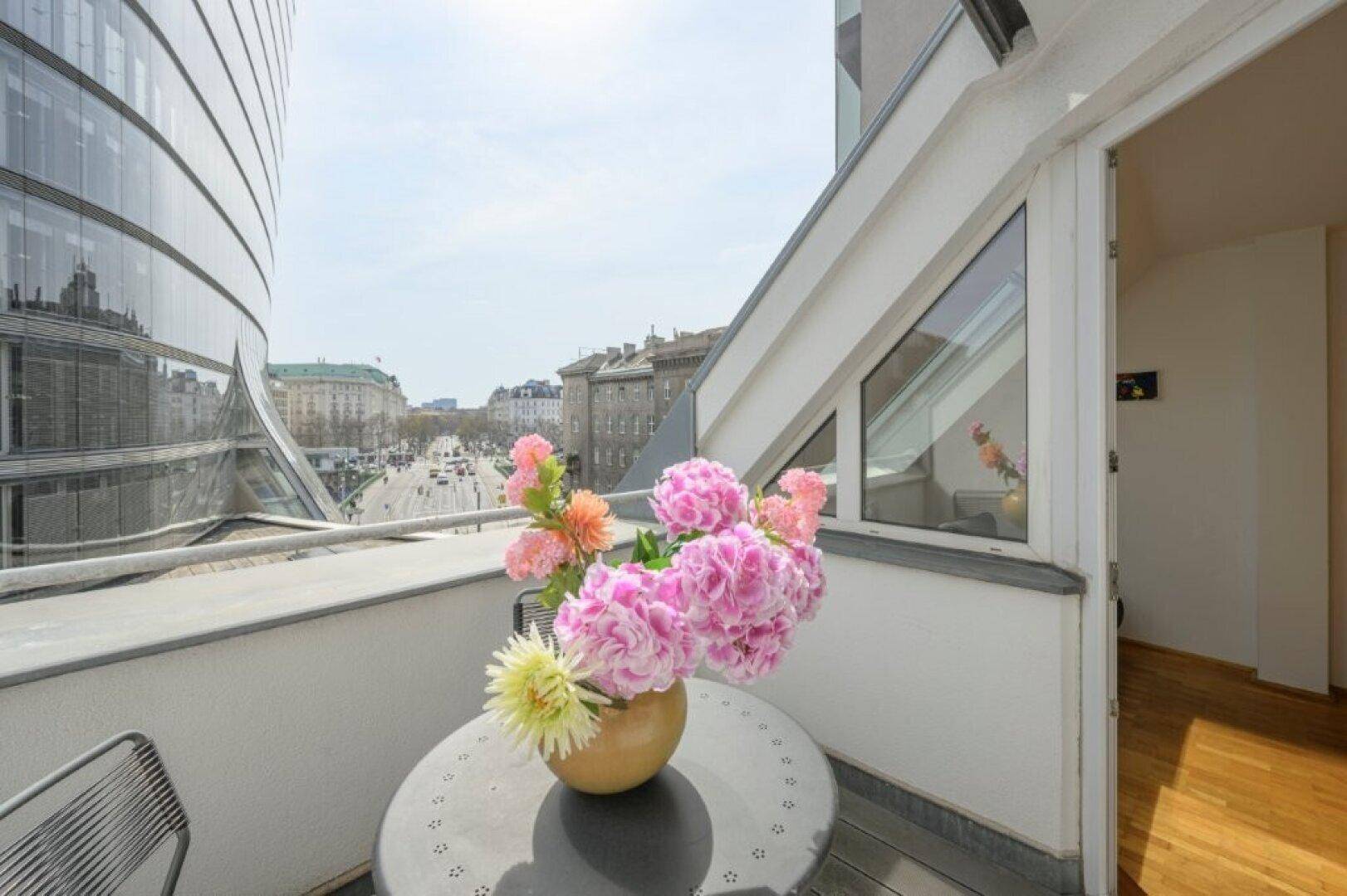 Balkon mit Stadtblick und Blumen, angrenzend an moderne Glasfassade.