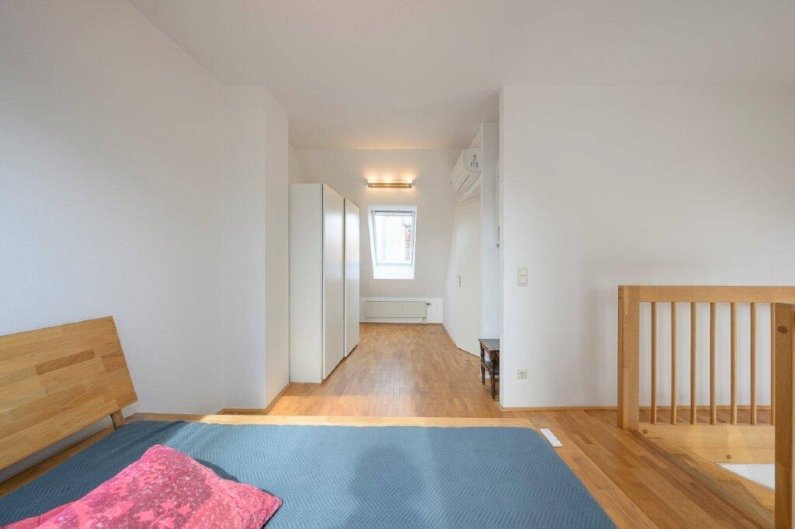 Schlafzimmer mit Holzbett, Einbauschränken und Dachfenster.