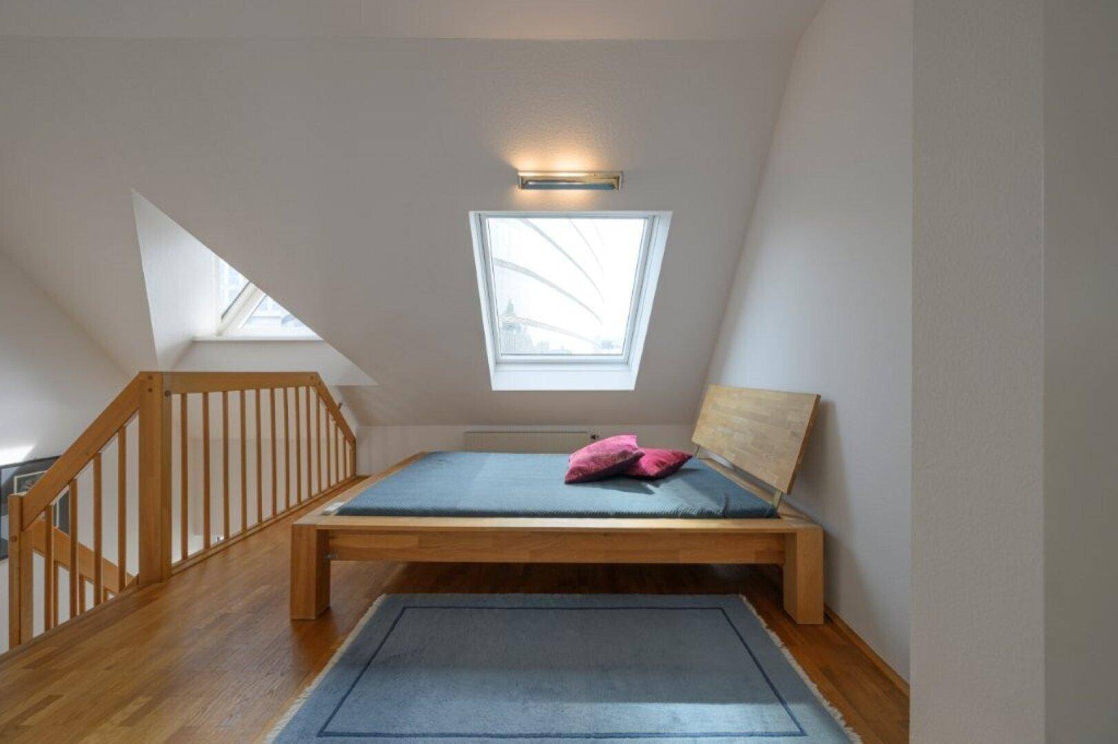 Schlafzimmer im Dachgeschoss mit Holzbett, Dachfenster und Holztreppe.