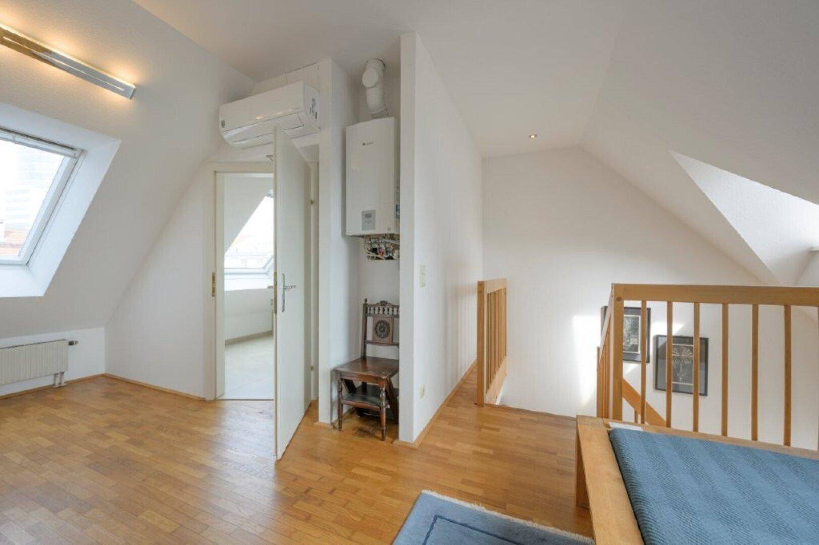 Schlafbereich im Dachgeschoss mit Holzbett, Heizung und Blick auf die Treppe.
