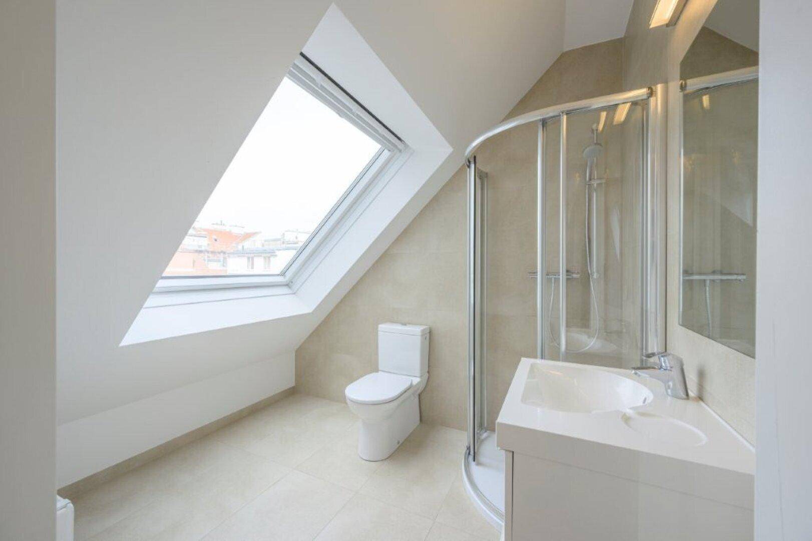 Modernes Badezimmer im Dachgeschoss mit Dusche, WC und Dachfenster.