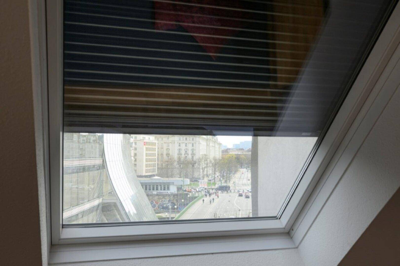 Dachfenster mit Rollladen und Blick auf die belebte Stadtstraße.