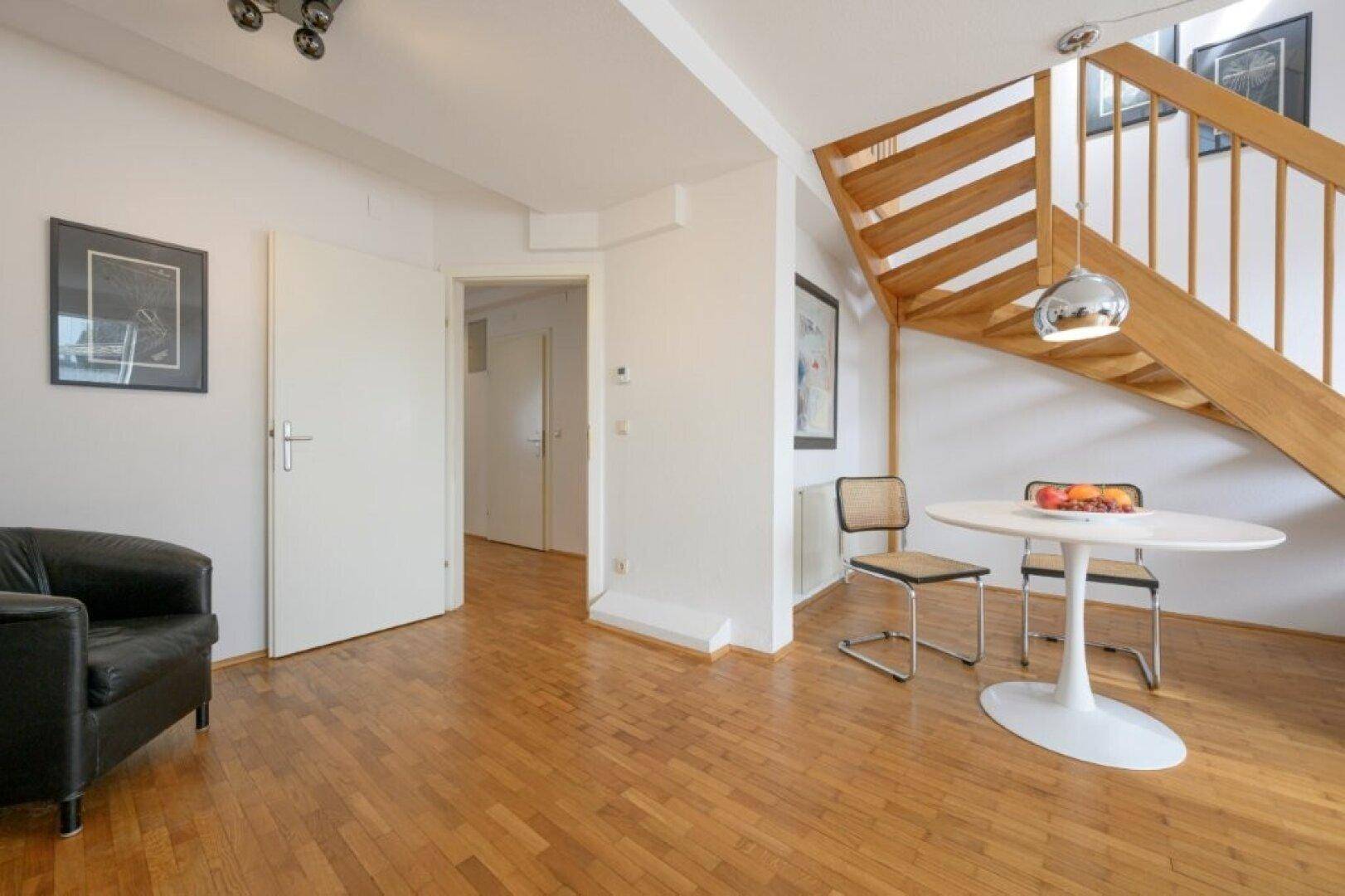 Wohnzimmer mit Parkettboden, Ledersessel und Zugang zu weiteren Räumen.