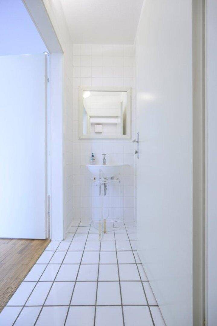 Heller Flur mit Fliesenboden, Waschbecken und Spiegel.