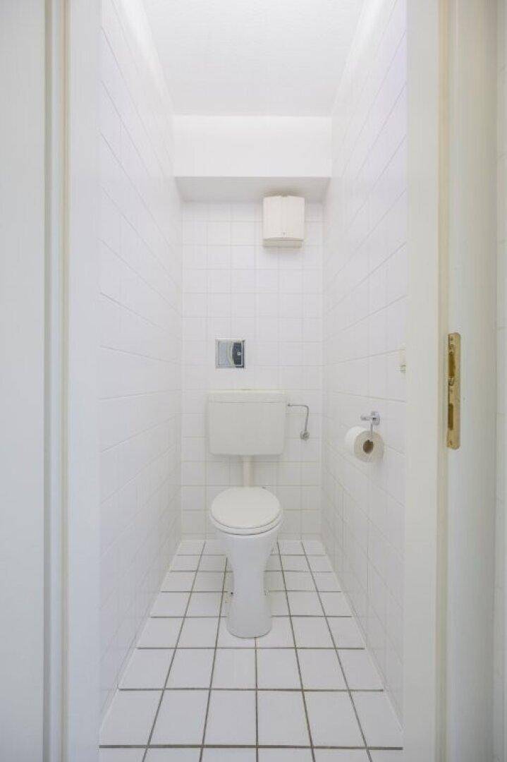 Kleines, hell gefliestes Gäste-WC mit Toilette und Fliesenboden.