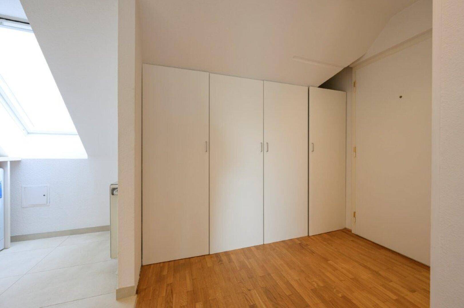 Schlafzimmer mit Einbauschränken unter der Dachschräge und Parkettboden.