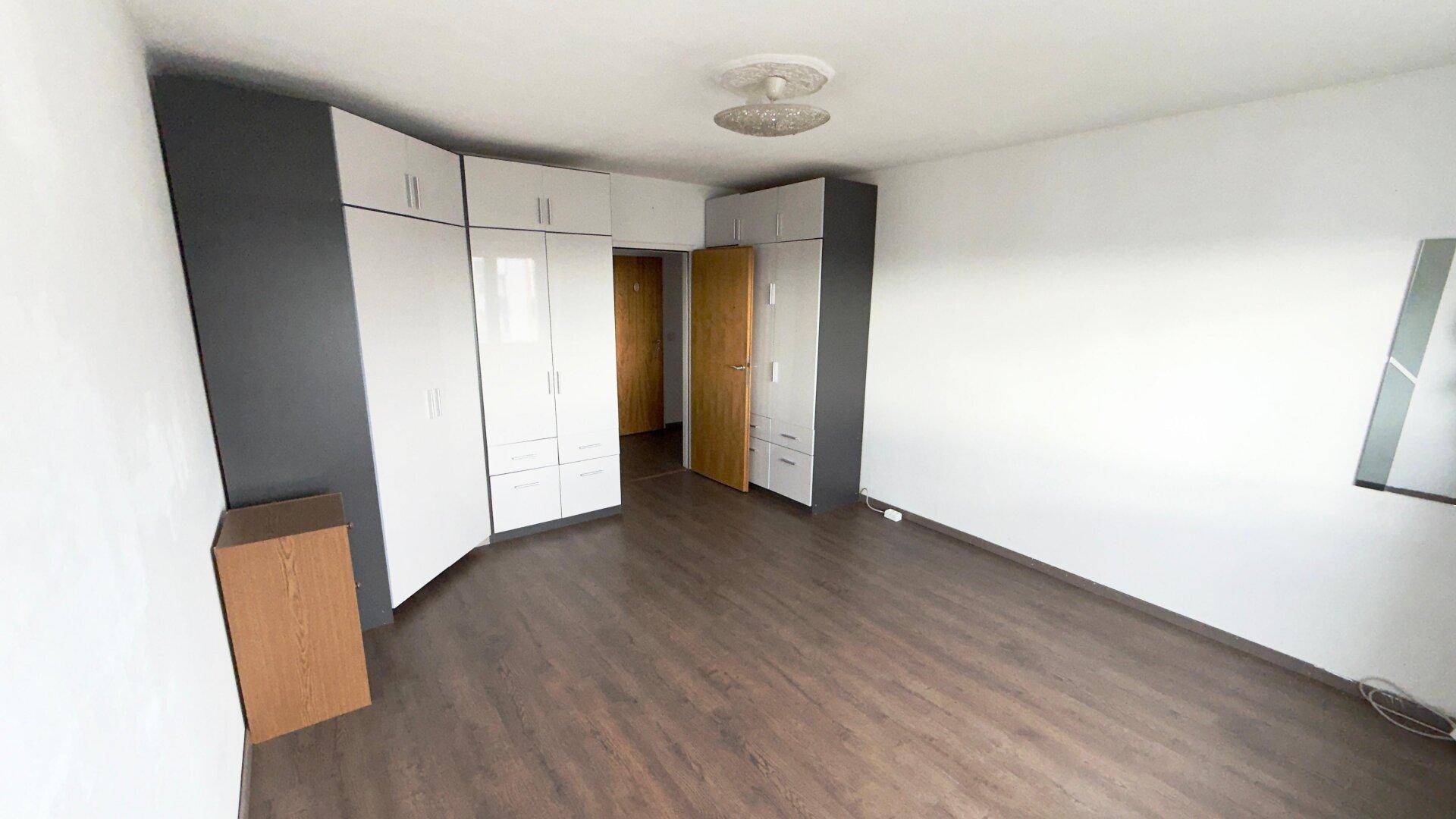 Helles Schlafzimmer mit großem Eckkleiderschrank in Weiß und Grau sowie dunklem Laminatboden.