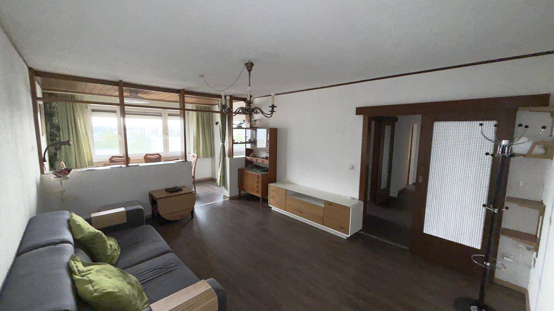 Geräumiger Wohnbereich mit Sofa, Kronleuchter und offenem Übergang zum Essbereich, ideal für geselliges Beisammensein.
