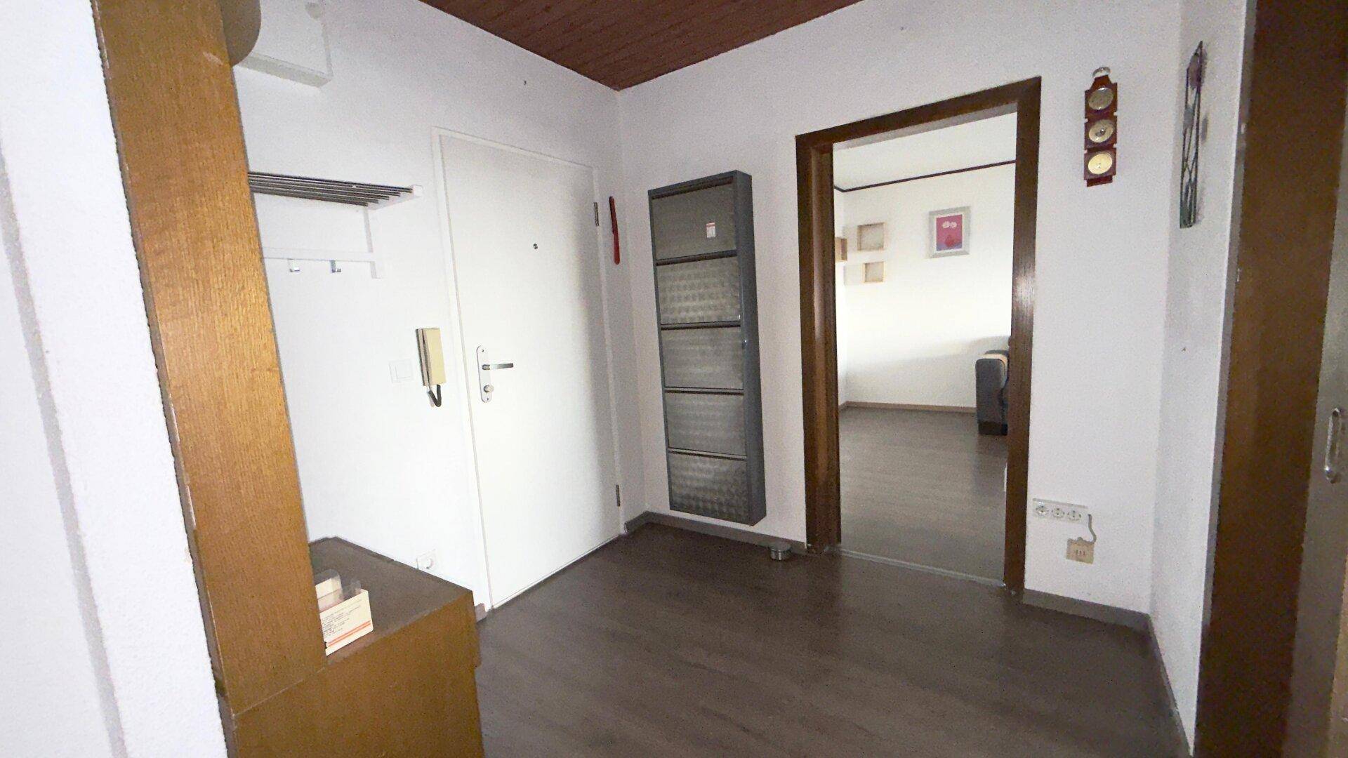 Eingangsbereich mit Haustür, Schuhregal und Garderobe, der einen Blick in den Wohnbereich freigibt.