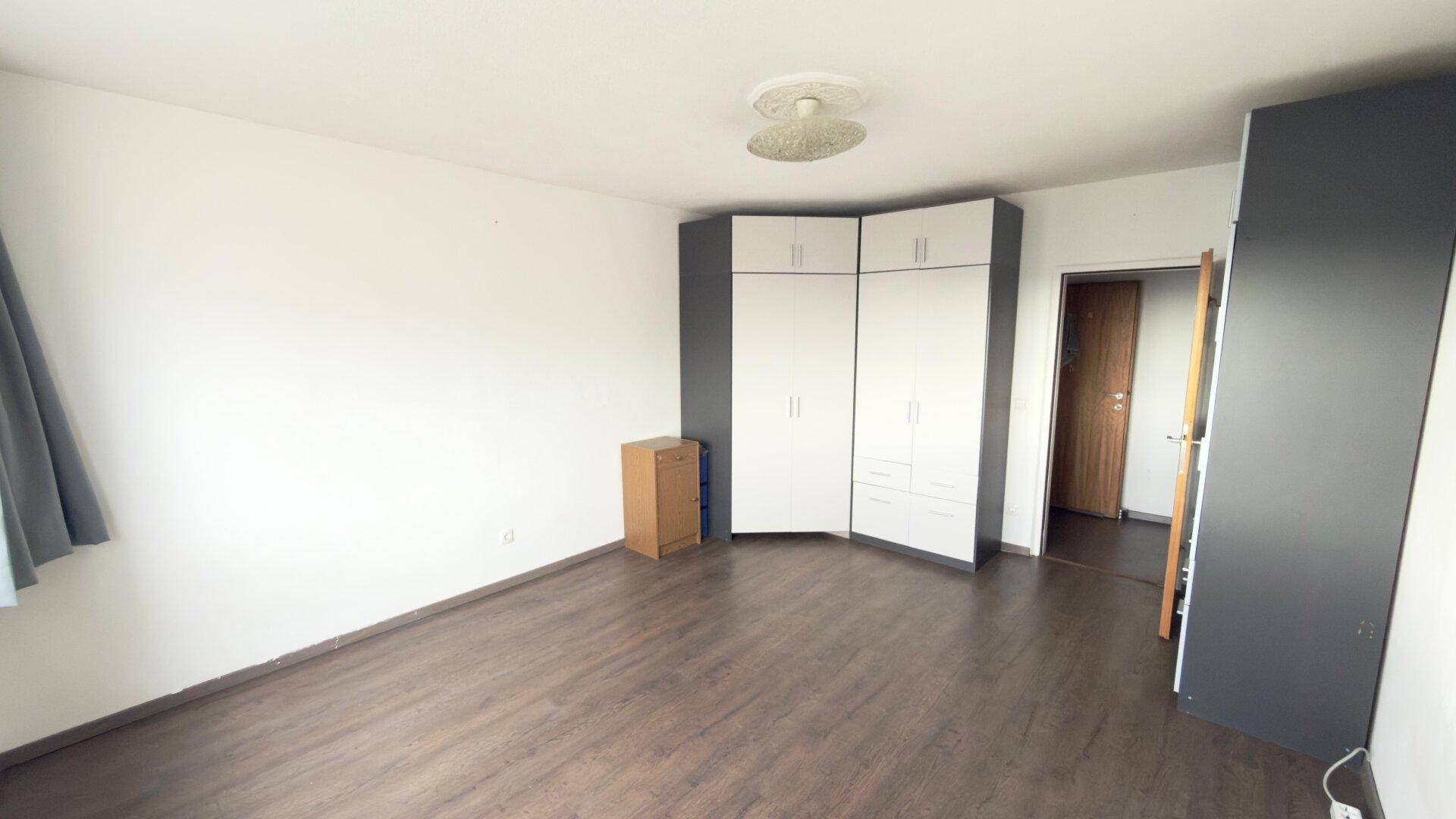 Geräumiges Schlafzimmer mit modernem Eckkleiderschrank und dunklem Laminatboden, ideal für individuelle Einrichtung.