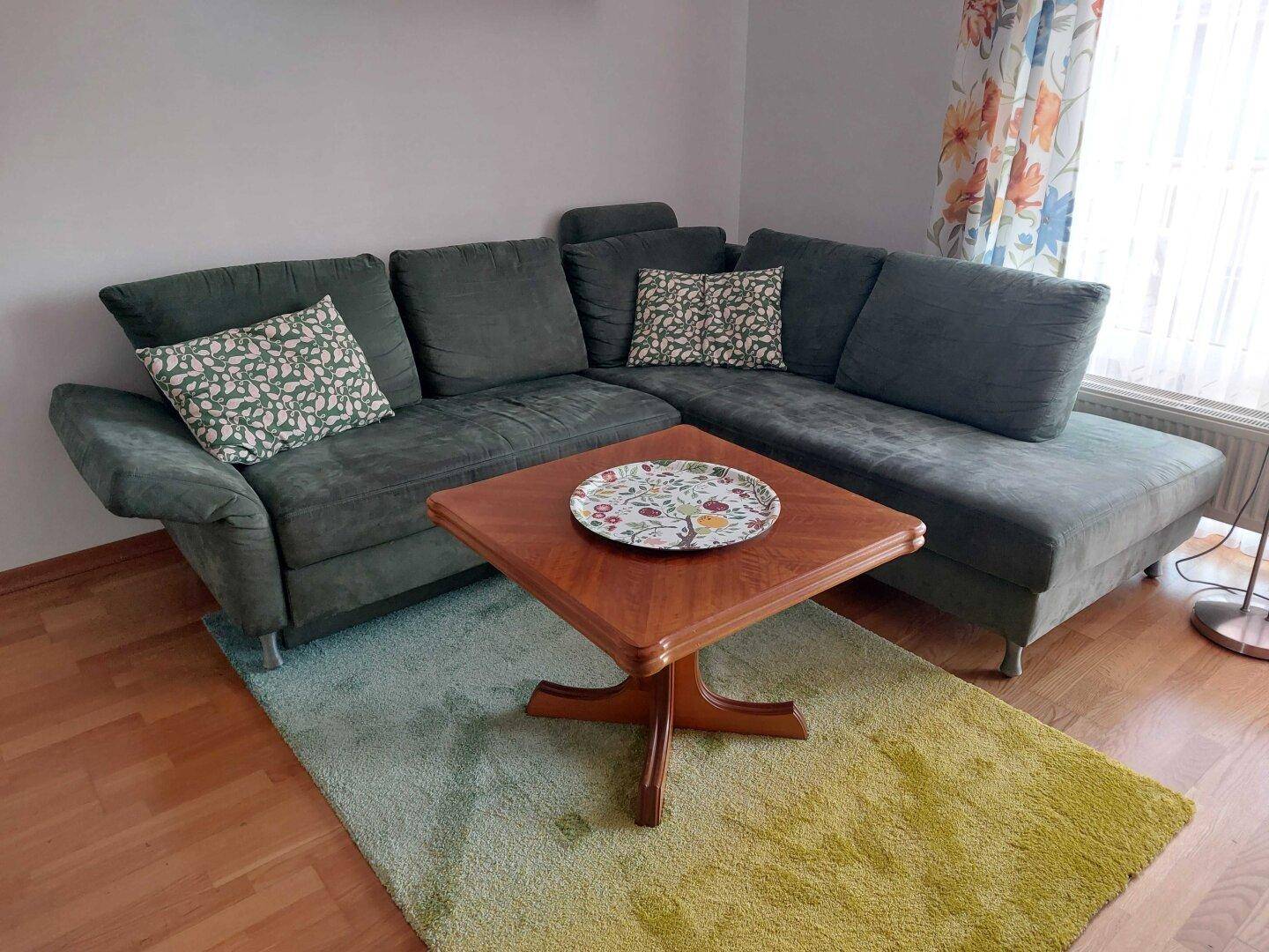 Gemütliches Wohnzimmer mit einem großen Ecksofa, Holztisch und farbenfrohem Teppich auf Parkettboden.