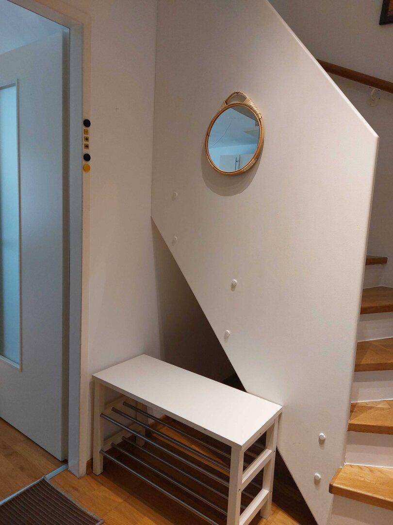 Eingangsbereich mit Holztreppe, Schuhregal und einem runden Spiegel an der Wand.
