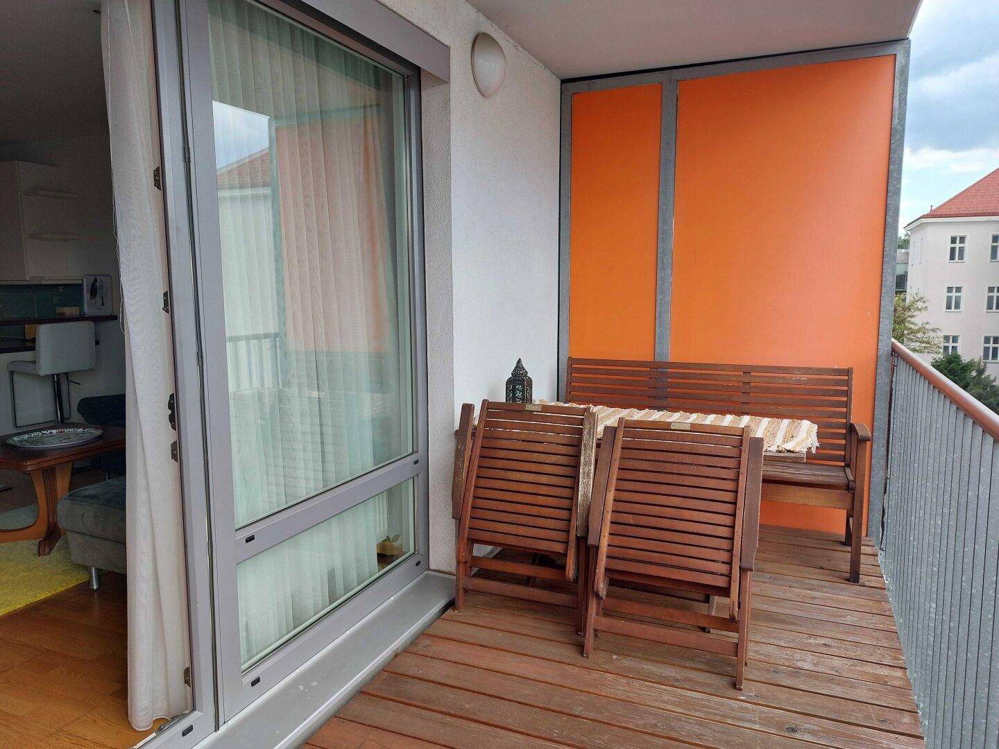 Gemütlicher Balkon mit Holzfußboden, Sitzbank und Klappstühlen, ideal zum Entspannen.