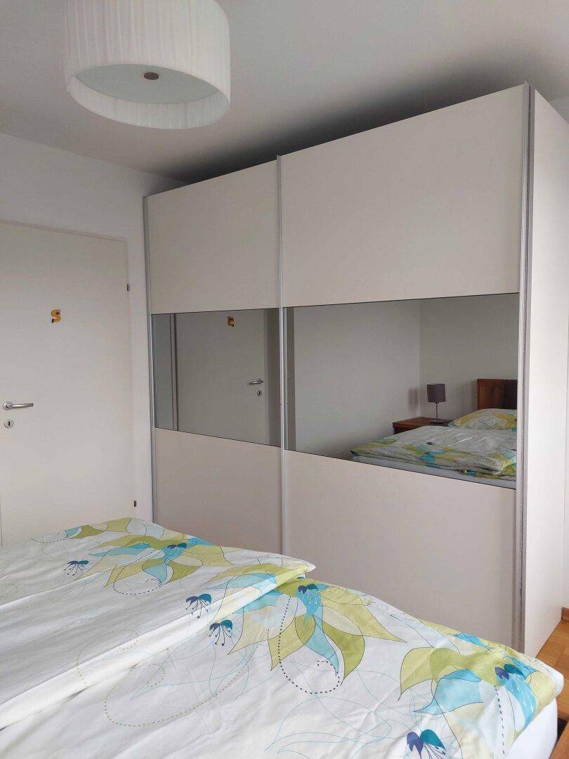 Schlafzimmer mit großem, weißem Kleiderschrank mit Spiegeltüren und Doppelbett.