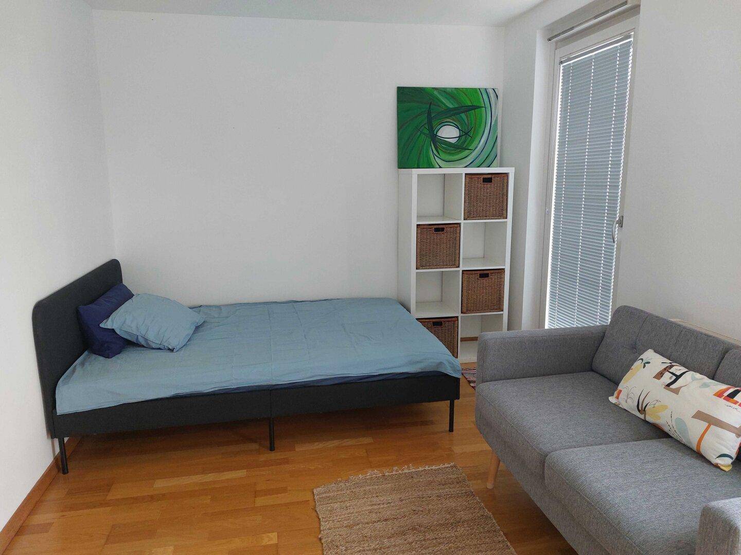 Helles Zimmer mit Einzelbett, kleinem Sofa und Regal, ideal als Gäste- oder Arbeitszimmer nutzbar.