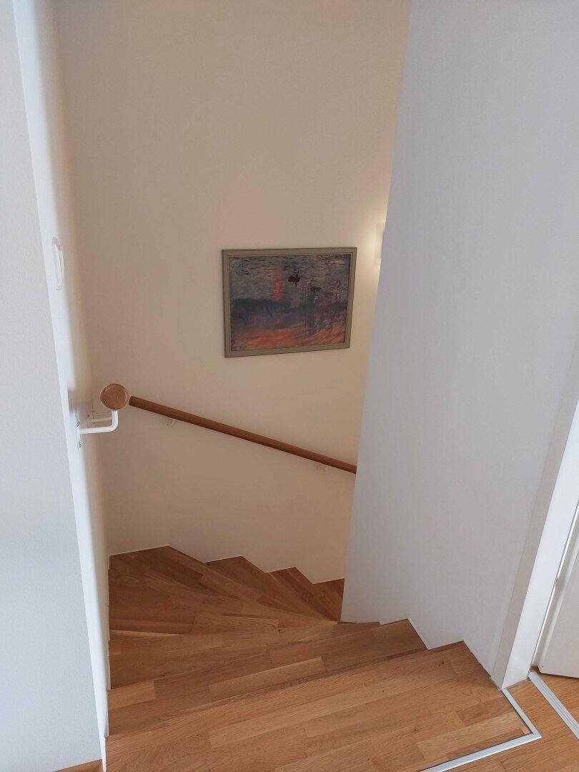 Holztreppe mit Handlauf führt in die obere Etage, ergänzt durch ein Wandbild.
