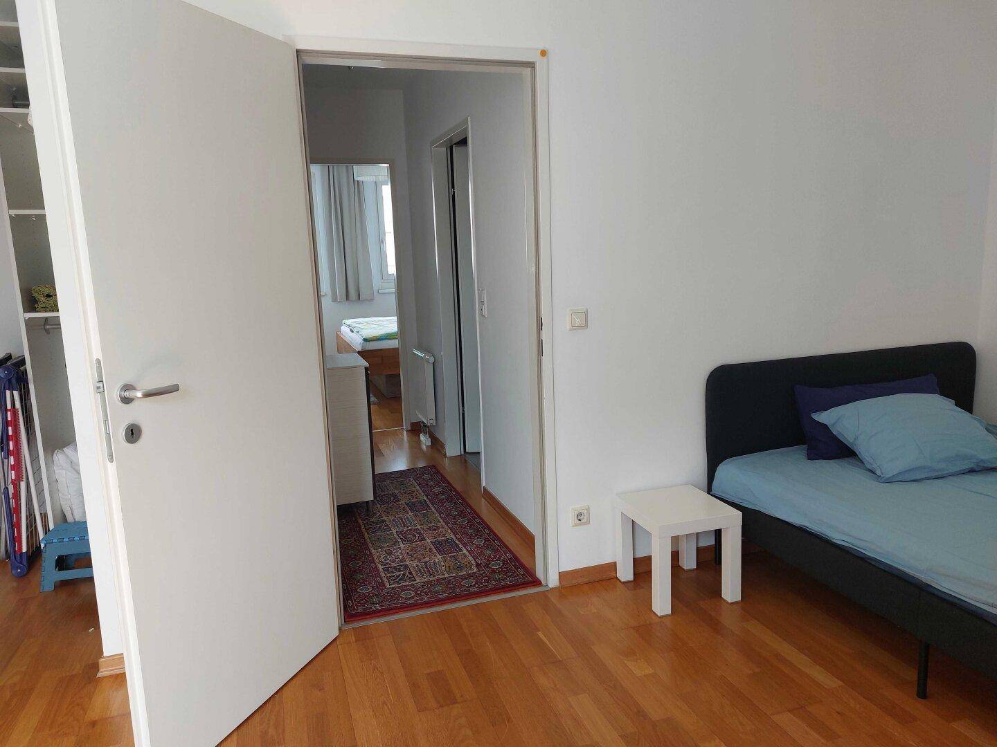 Blick aus einem Zimmer in einen weiteren Schlafbereich mit Bett und Holzboden.