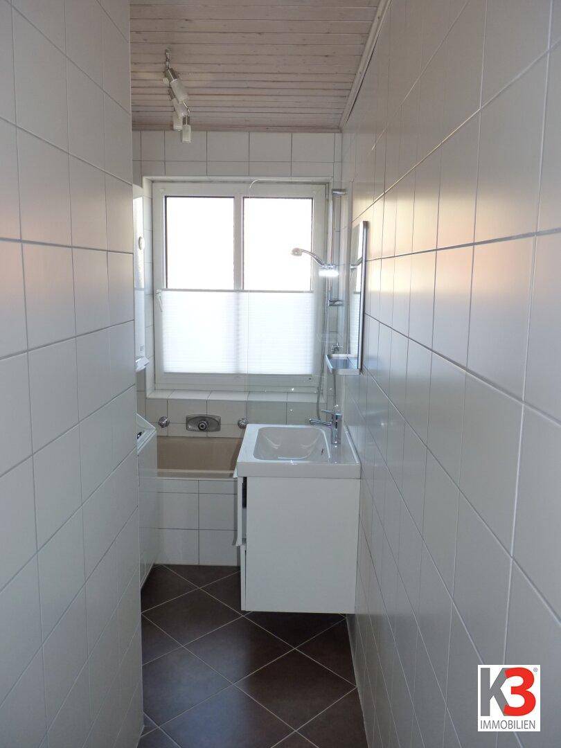 Schlichtes Badezimmer mit weißen Wandfliesen, dunklem Boden und einer Badewanne mit Duschfunktion.
