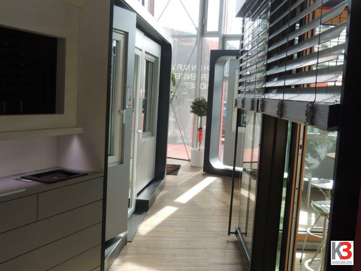 Moderner Flur oder Ausstellungsbereich mit großen Fenstern, Jalousien und zeitgenössischen Designelementen.