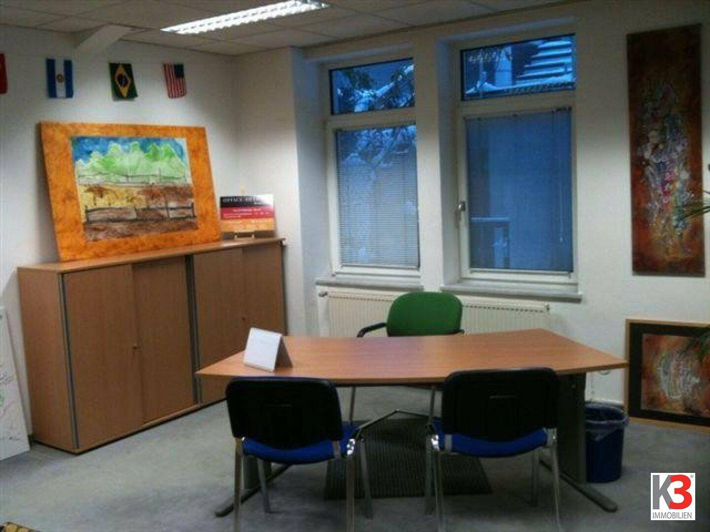 Helles Büro mit Schreibtisch, zwei Stühlen und einem Fenster mit Blick nach draußen.
