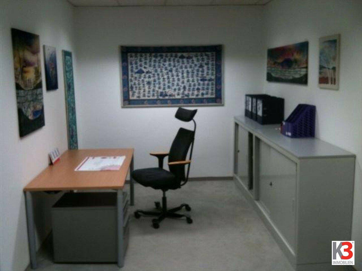 Kleines Büro mit Schreibtisch, Bürostuhl und einem grauen Aktenschrank an der Wand.