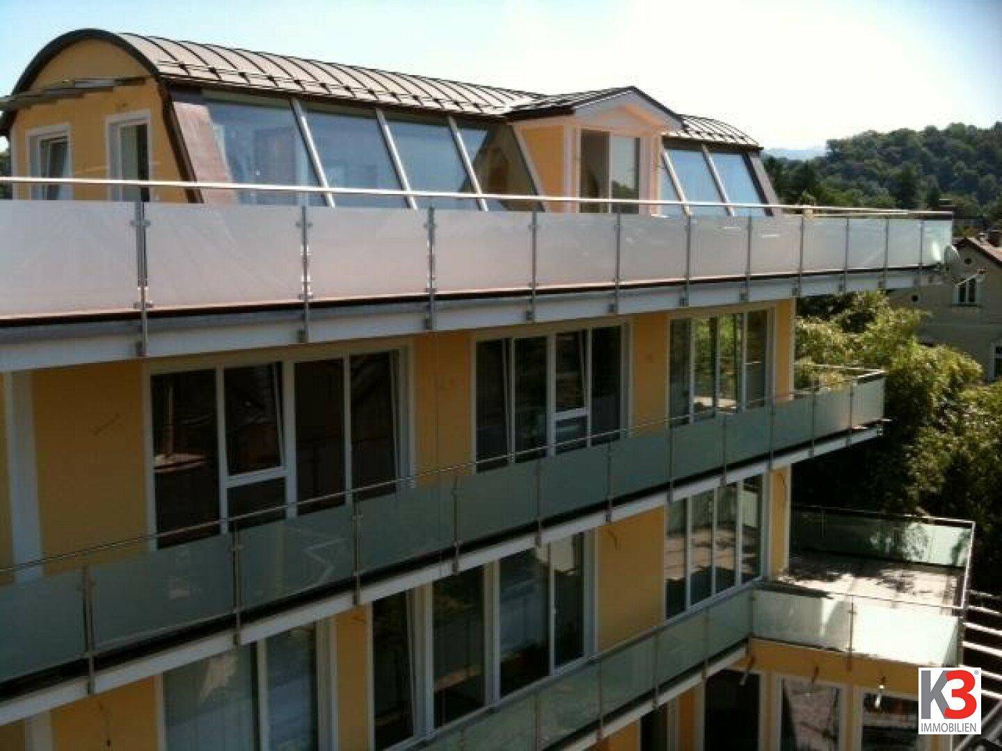 Fassade eines gelben Gebäudes mit mehreren Balkonen und großen Glasfronten bei Sonnenschein.