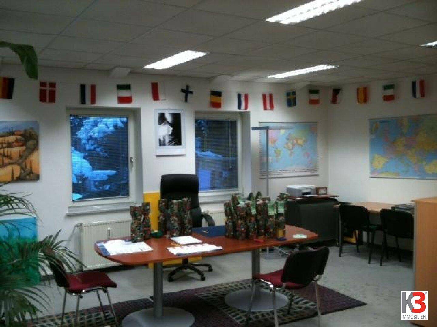 Geräumiges Büro mit mehreren Arbeitsplätzen, Fenstern und einer Dekoration aus Länderflaggen.