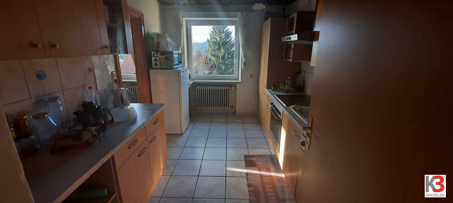 Kleine, funktionale Küche mit Fliesenboden, Holzschränken und Fenster mit Ausblick.