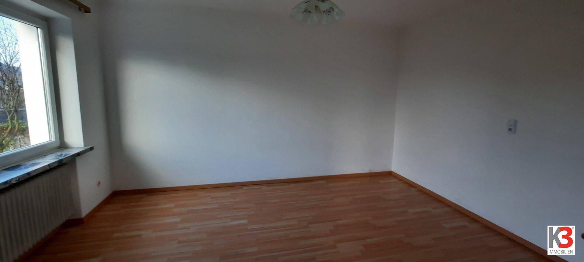 Leeres, helles Zimmer mit Laminatboden und großem Fenster, vielseitig nutzbar.