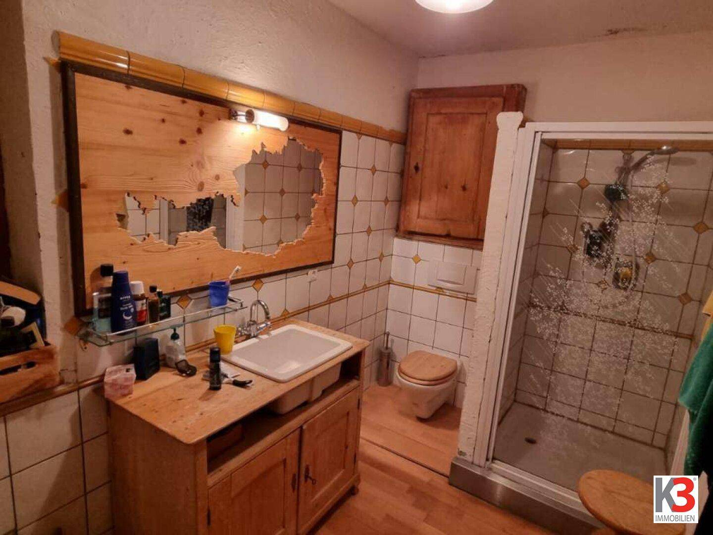 Badezimmer mit Duschkabine, WC, Waschbecken auf Holzunterschrank und gefliesten Wänden.